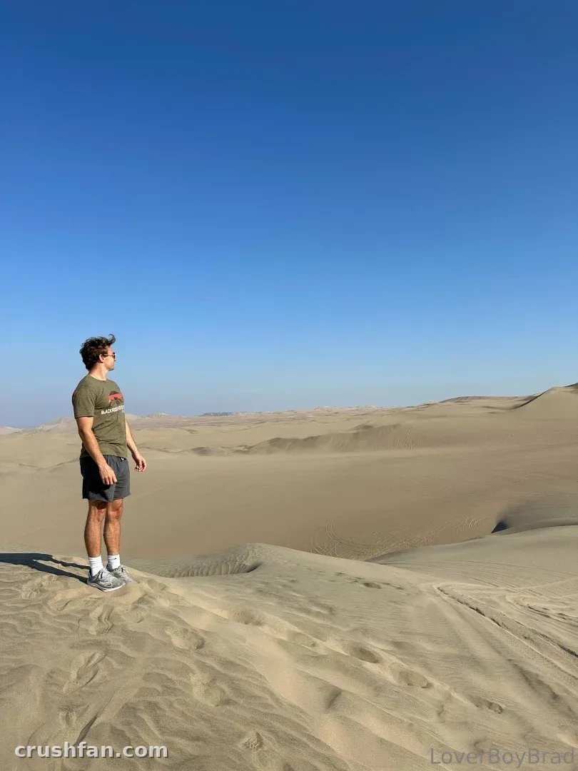 Leo steht auf einer Sanddüne und trägt ein grünes T-Shirt und eine Shorts unter einem klaren blauen Himmel.