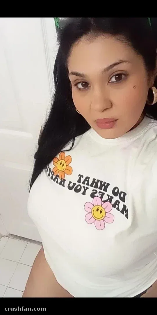 Beautybygen dans un t-shirt graphique blanc avec imprimé floral, prenant un selfie rapproché en intérieur.