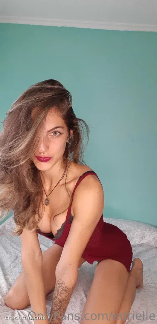 Edrielle kneeling on a bed in a burgundy bodysuit against a teal wall