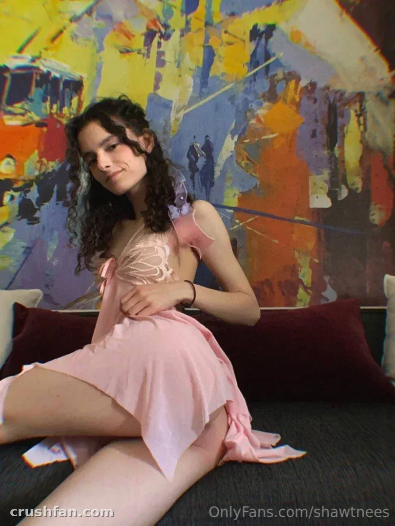 Nestix💕 in a pink slip dress seated on a sofa in front of a colourful abstract painting