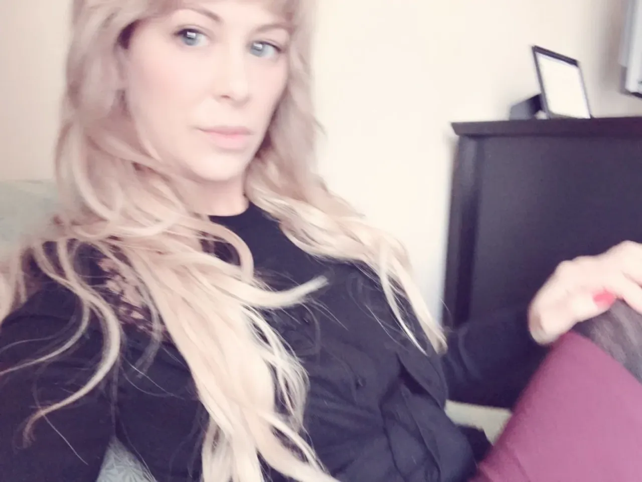 Cherie DeVille con un top negro y leggings burdeos sentada en interiores