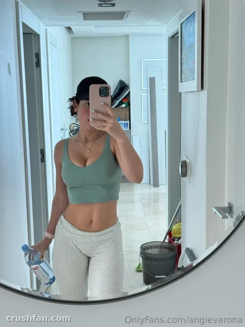 Angie Varona tirando uma selfie no espelho com um top verde e leggings cinza.