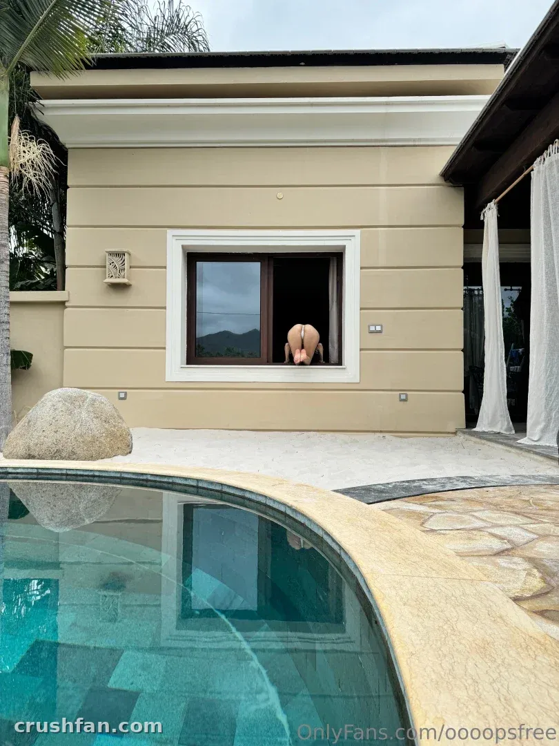 Personne à une fenêtre de villa au-dessus d'une piscine turquoise avec bord en pierre et palmes