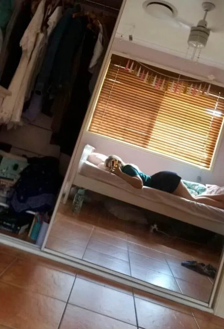 Shel ♡ lying on a bed, viewed through a mirror in a softly lit room.