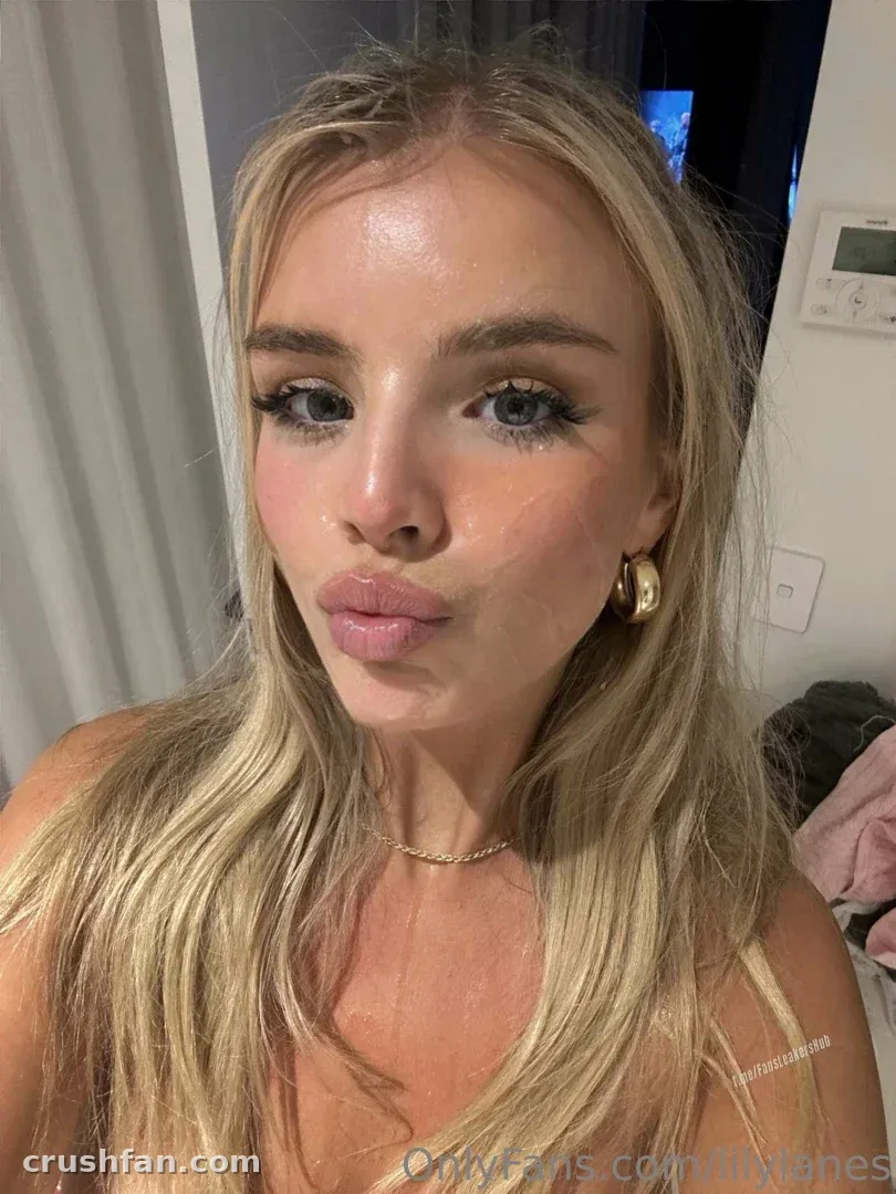Close-up selfie of Lily Lanes with blonde hair, gold necklace and hoop earring indoors.