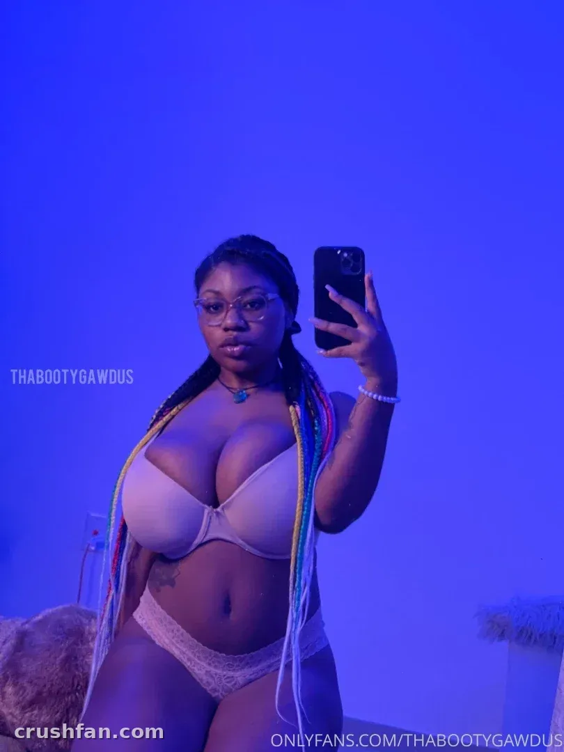 Destiny Skie in a blue-lit room taking a mirror selfie in light lingerie with colourful braids
