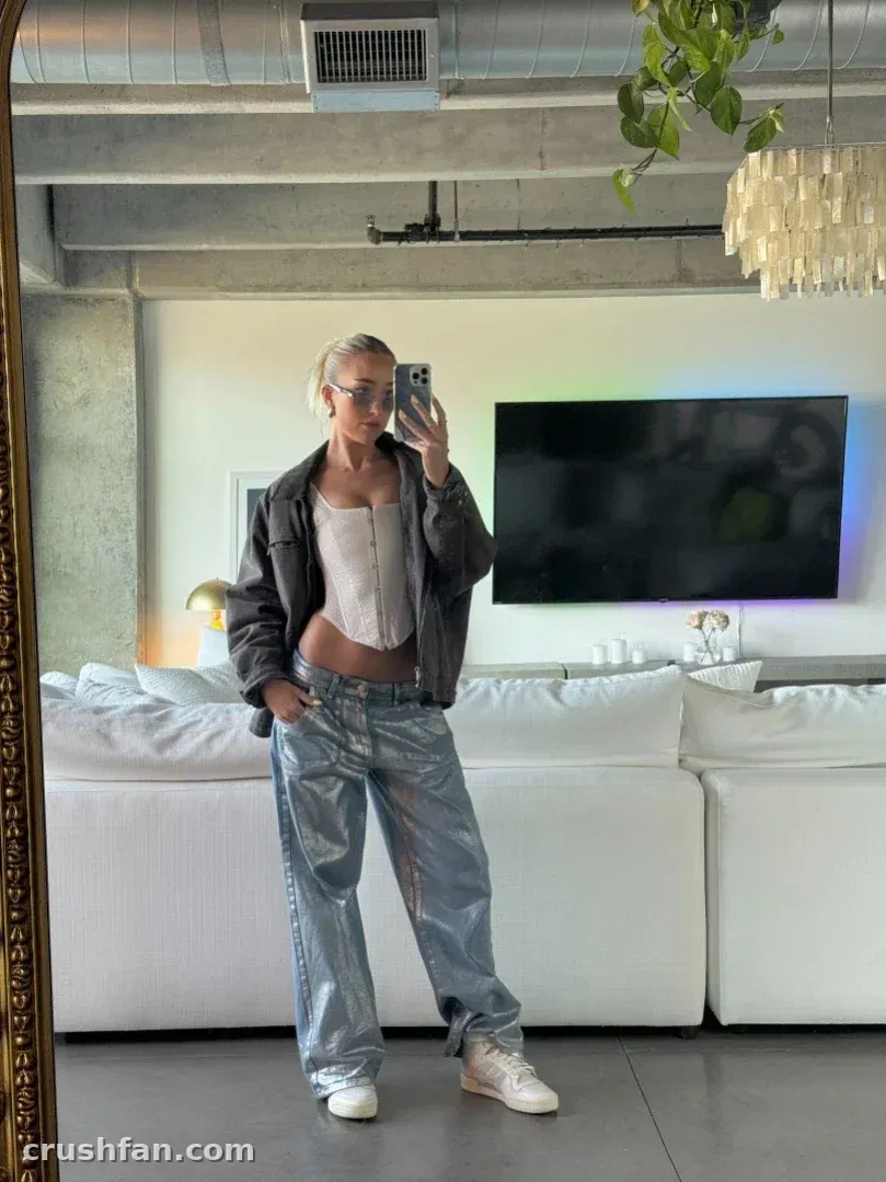 Madds prend un selfie dans le miroir dans un salon loft lumineux, portant une veste et un pantalon bleu clair.