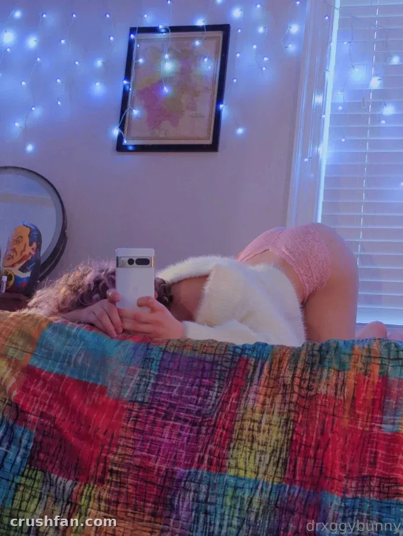 Vinny está deitada em uma cama com um cobertor colorido, segurando um telefone sob luzes de fada azuis.