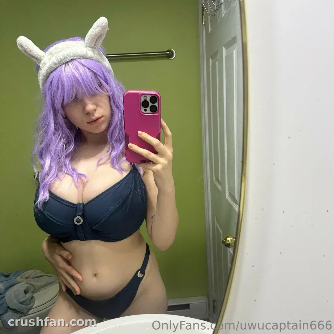 Touki00 con peluca morada y orejas blancas tomándose una selfie en el espejo en un baño verde.