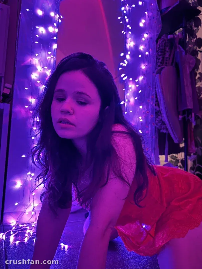 Creator in a red top leaning forward in a room lit by purple and fairy lights.