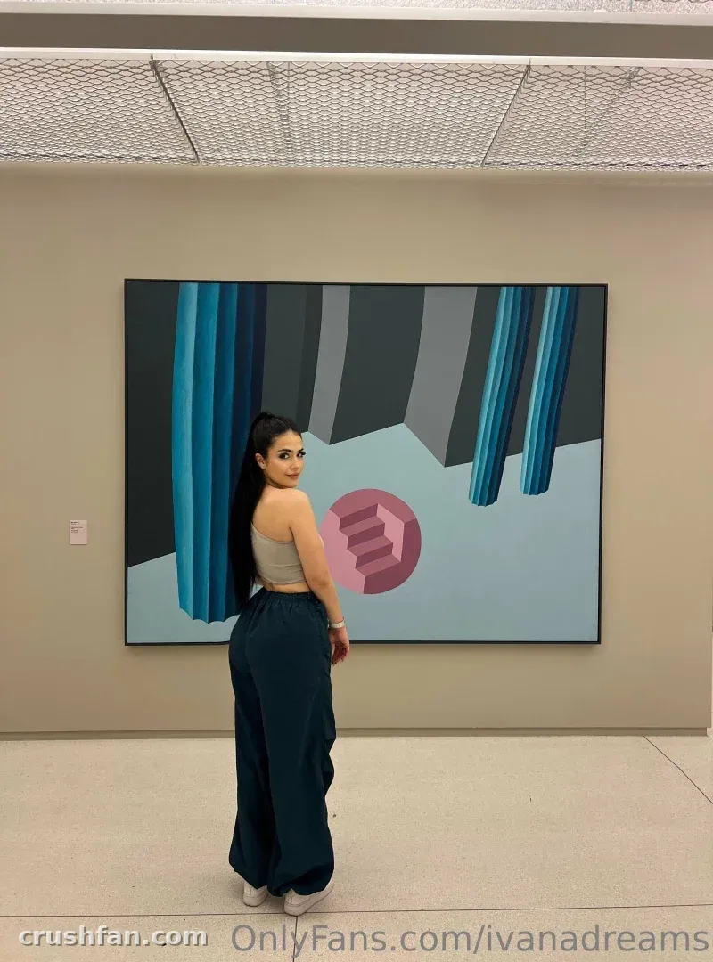 Femme en haut gris et pantalon bleu sarcelle debout devant une grande peinture abstraite dans une galerie