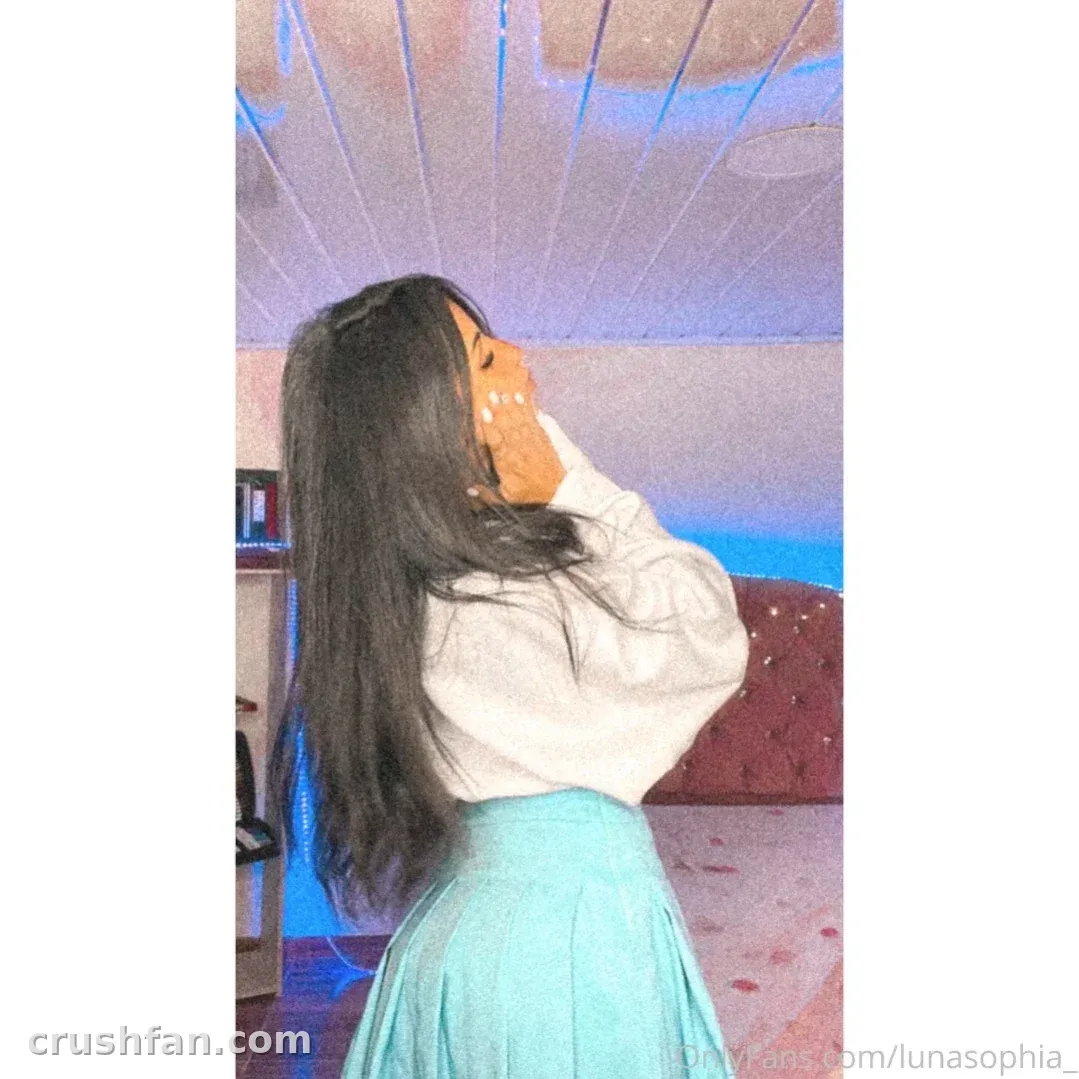 Luna Sophia com um top branco e saia verde-azulada em pé em ambiente interno sob luz azul