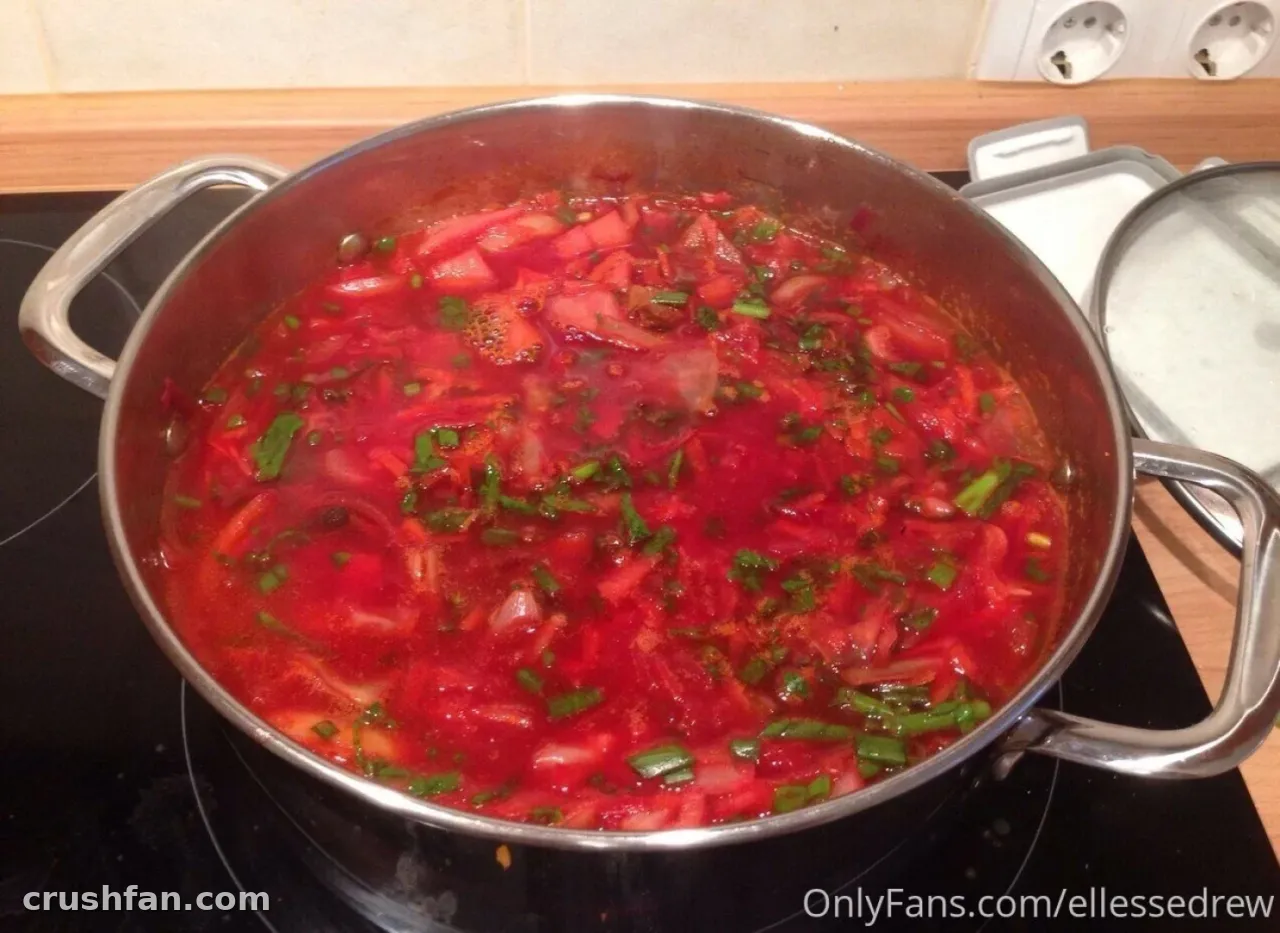 Olla grande de acero con sopa de verduras roja cubierta de hierbas verdes sobre una cocina negra