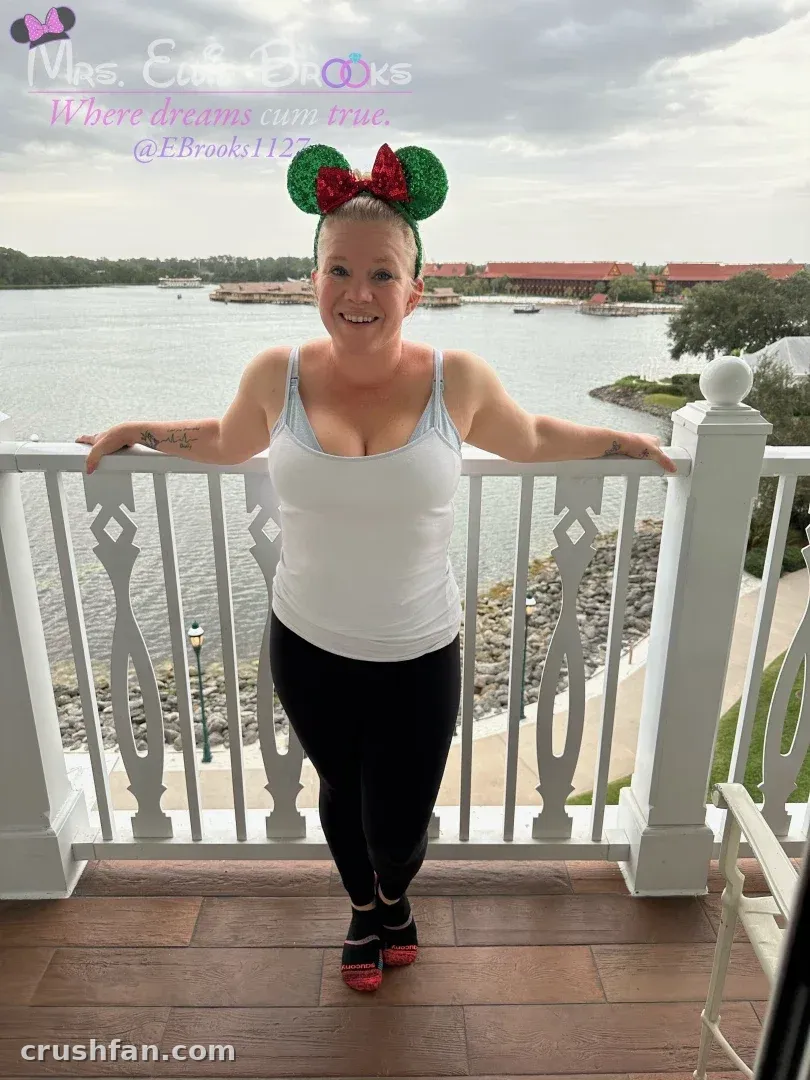 Ellie Brooks in einem weißen Tanktop und schwarzer Leggings auf einem Balkon am Wasser