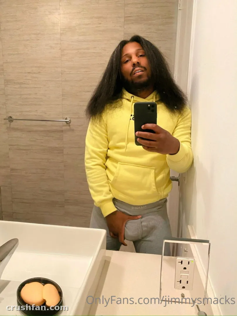 JimmySmacks in a yellow hoodie and grey sweatpants taking a mirror selfie in a tiled bathroom.