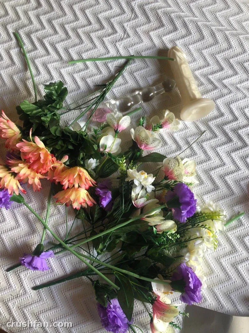 Overhead view of orange and purple flowers with a clear glass object on a white textured blanket