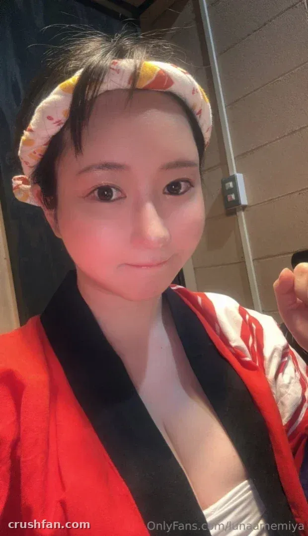 Luna Amemiya in a red robe and patterned headband taking a selfie indoors.