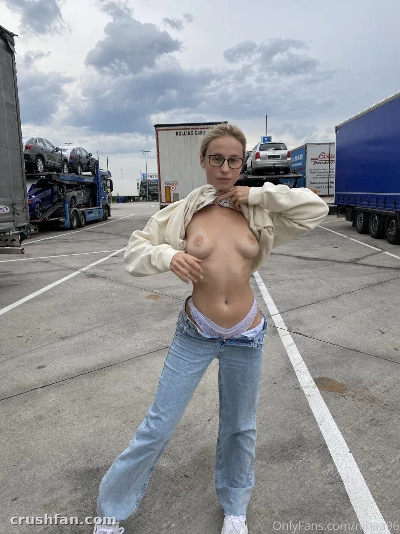 Nina Joy standing in a paved truck yard wearing an open cropped jacket and light blue jeans