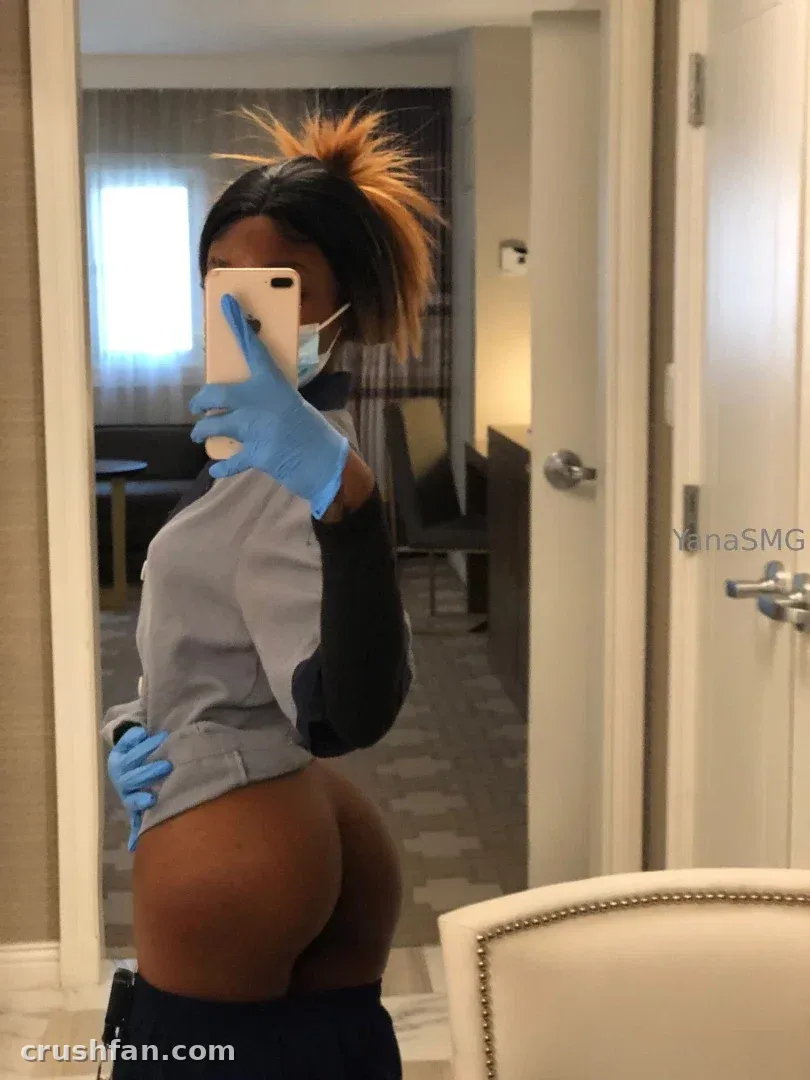 YanaSMG macht ein Spiegel-Selfie in einem Hotelzimmer, trägt ein graues Oberteil und einen orangefarbenen Pferdeschwanz.