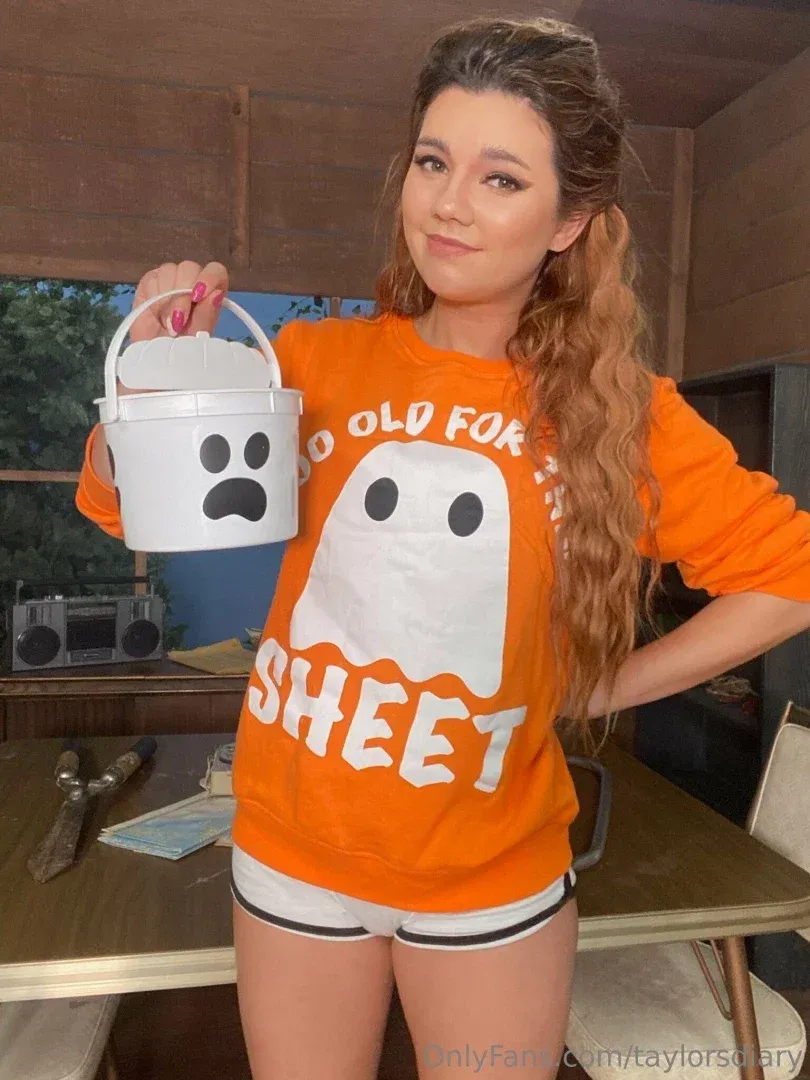 Taylor’s diary in an orange ghost shirt holding a white ghost bucket indoors.
