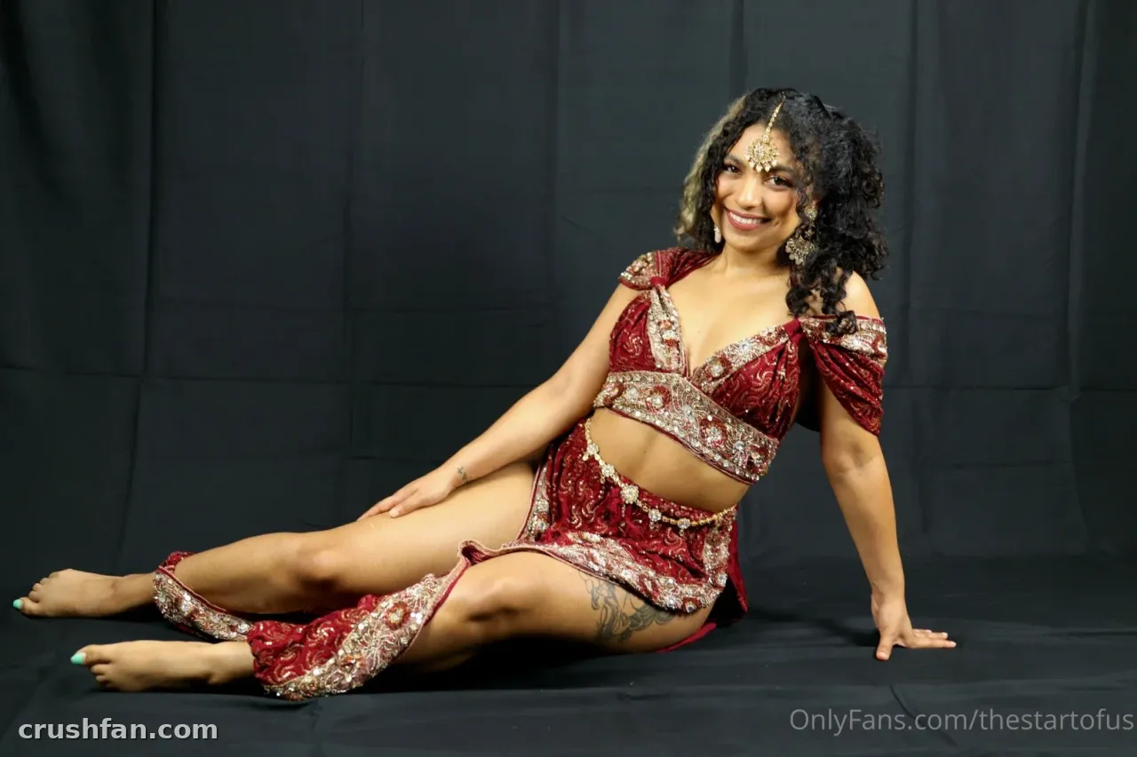 Creator seated on the floor in a red embellished two-piece outfit against a dark backdrop