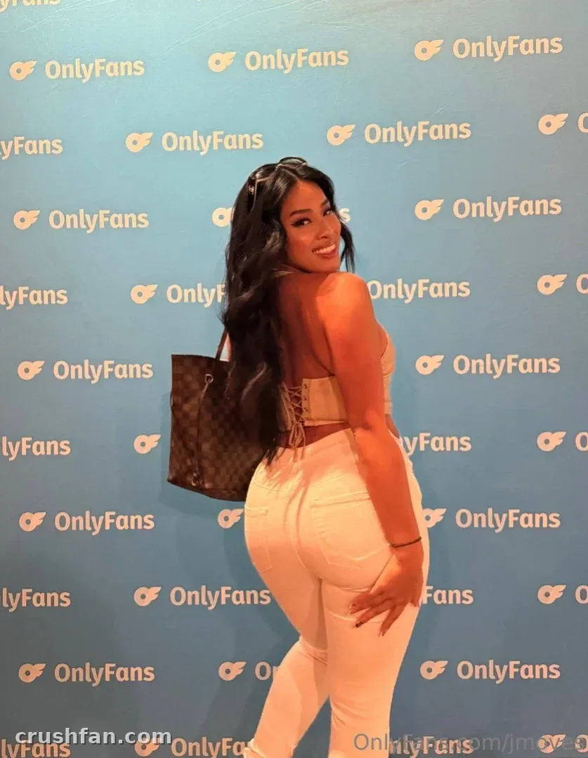 Jade smiles over her shoulder in a cream outfit against a blue branded backdrop