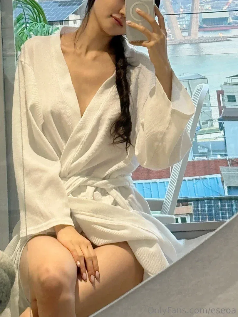 e_seoa de roupão branco tirando uma selfie no espelho perto de uma janela clara