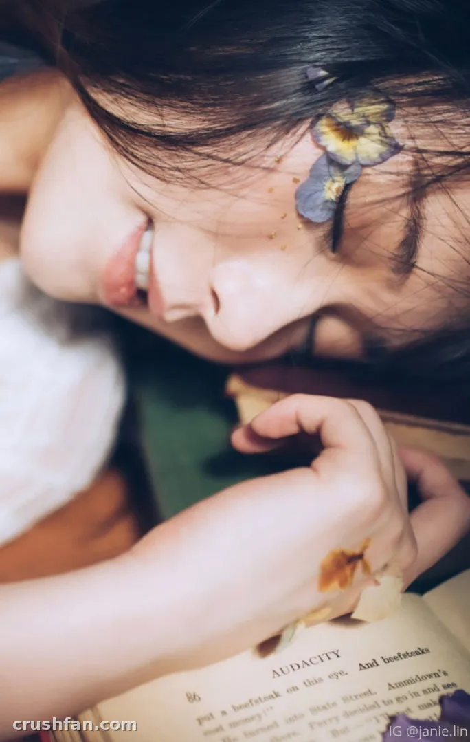 Creator descansando junto a un libro abierto con pequeñas flores prensadas cerca de su cabello