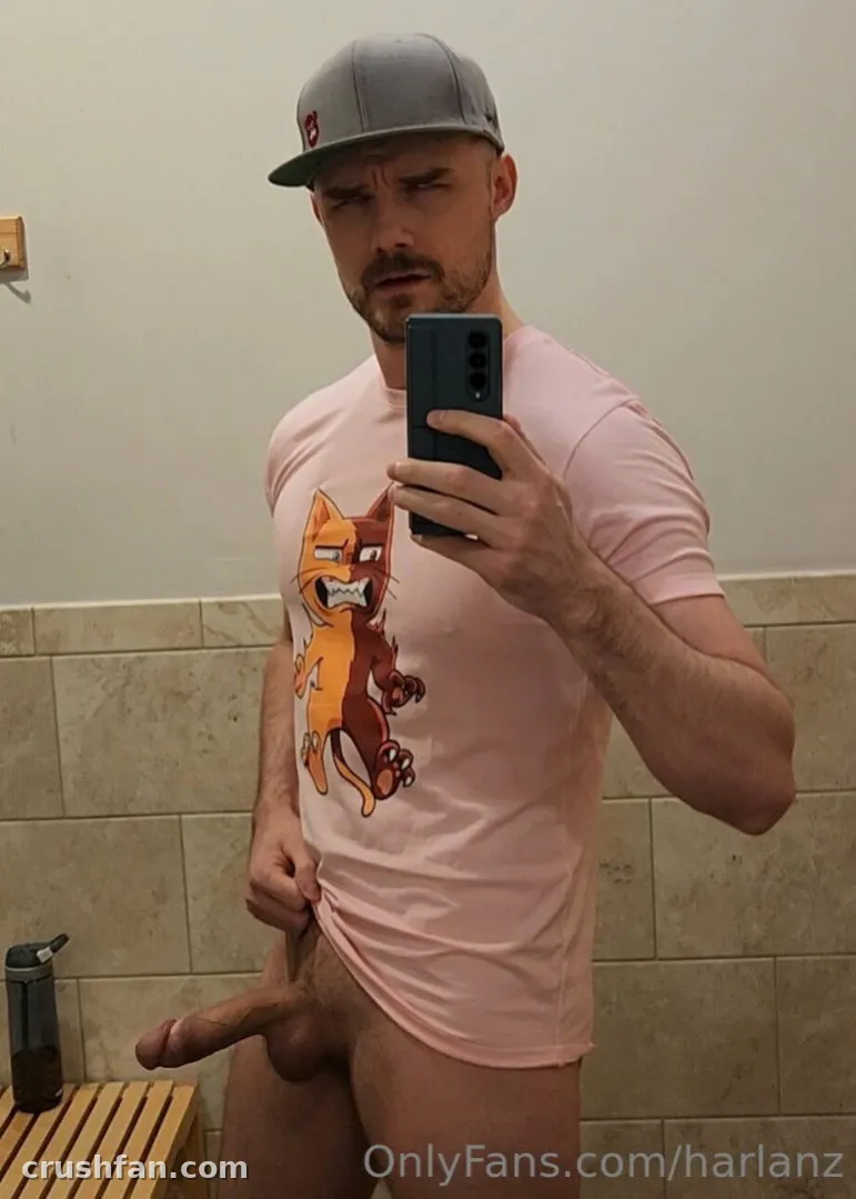 Harlan con gorra gris y camiseta rosa estampada de gato tomándose una selfie en el espejo del baño