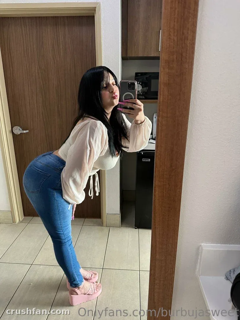 Tia Burbuja se toma un selfie de espejo con una blusa crema y jeans azules en interiores