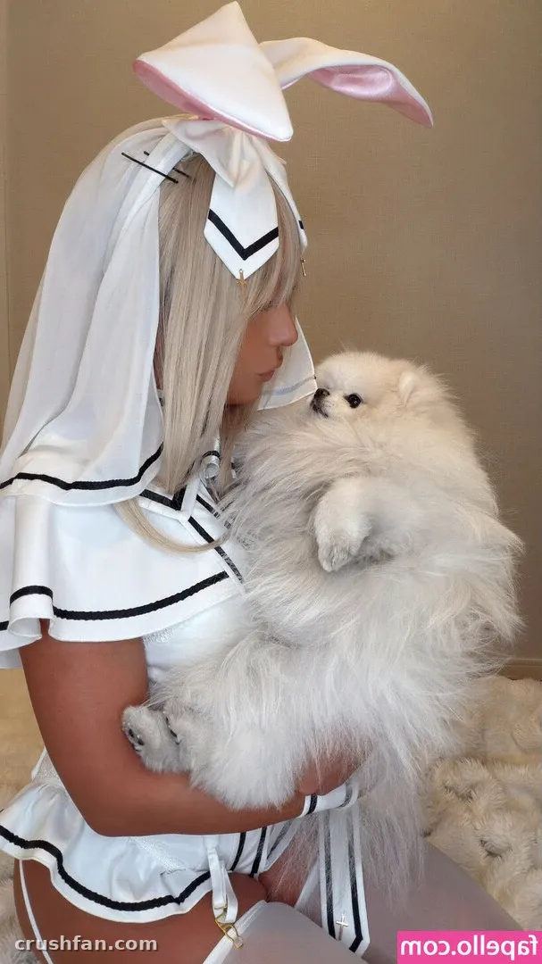 Creator in white sailor-style cosplay with rabbit-ear headpiece holding a fluffy white dog