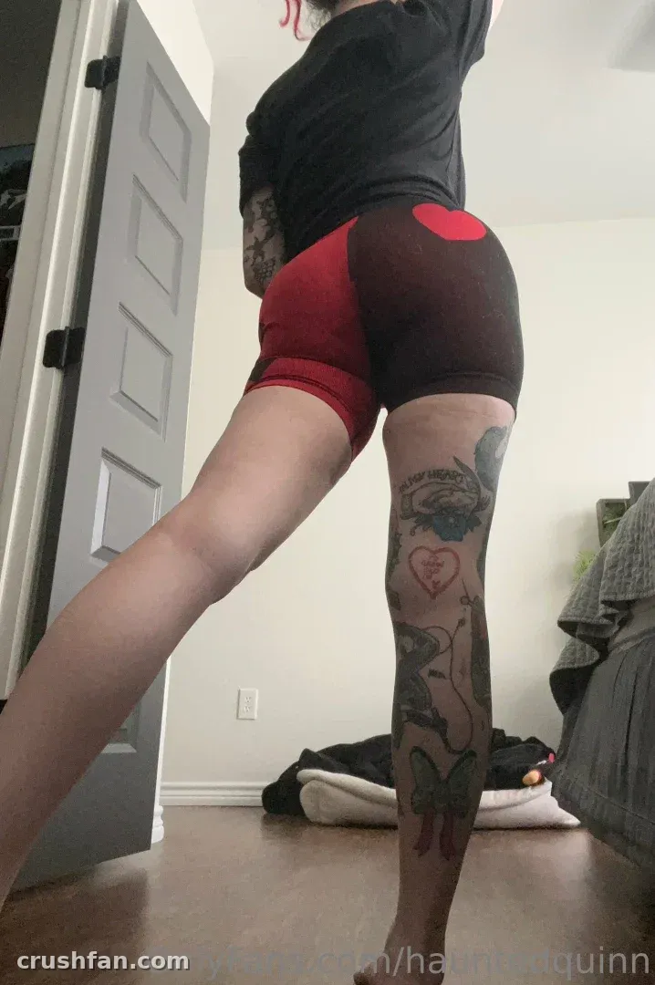 Haley Quinn de blusa preta e shorts mostrando as tatuagens da perna em ambiente interno