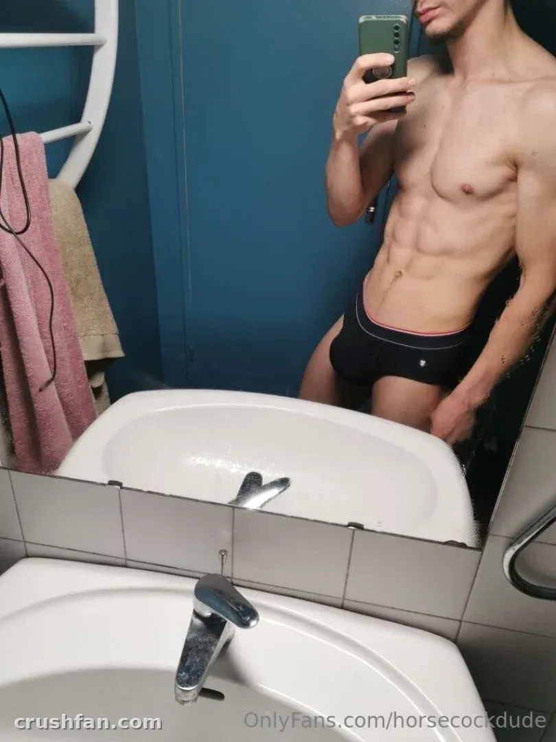 Horsecock dude takes a mirror selfie in a bathroom with a blue wall and white sink.