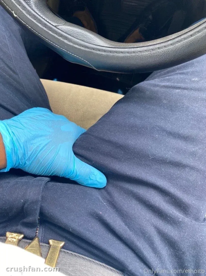 Close-up of a blue-gloved hand resting on navy trousers inside a car