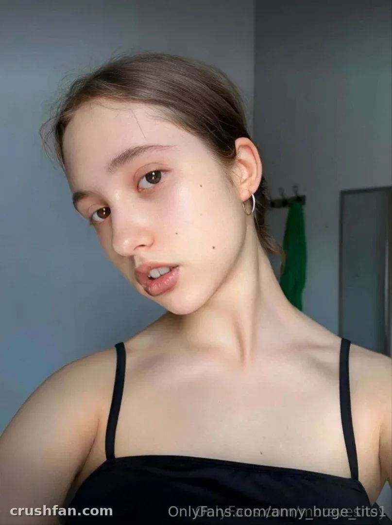Anny in a black top posing indoors against a grey wall