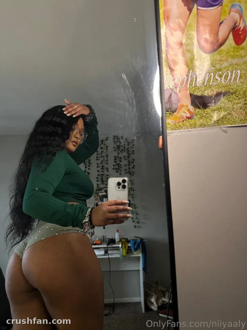 Criadora com um top cropped verde tirando uma selfie no espelho em um quarto com um pôster na parede