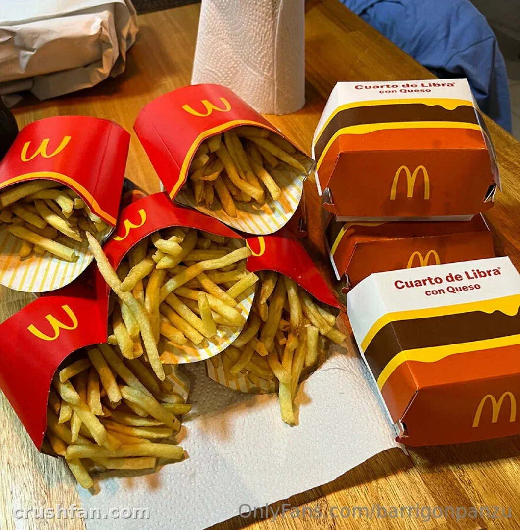 Caixas vermelhas de batatas fritas transbordando sobre papel ao lado de caixas de hambúrguer empilhadas em uma mesa de madeira