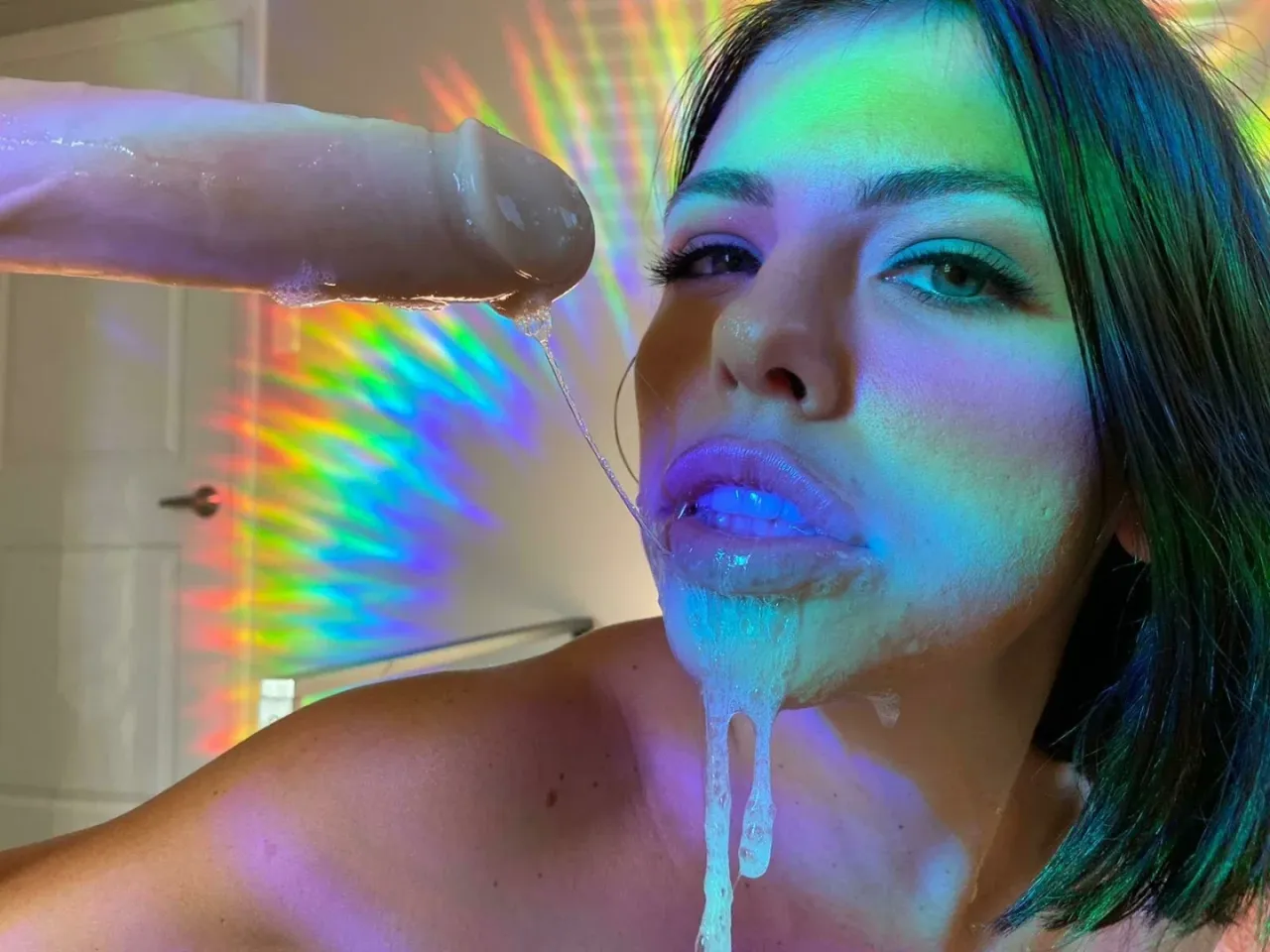 Adriana Chechik im Close-up unter regenbogenfarbenem Licht mit einem glänzenden Strahl an ihren Lippen.