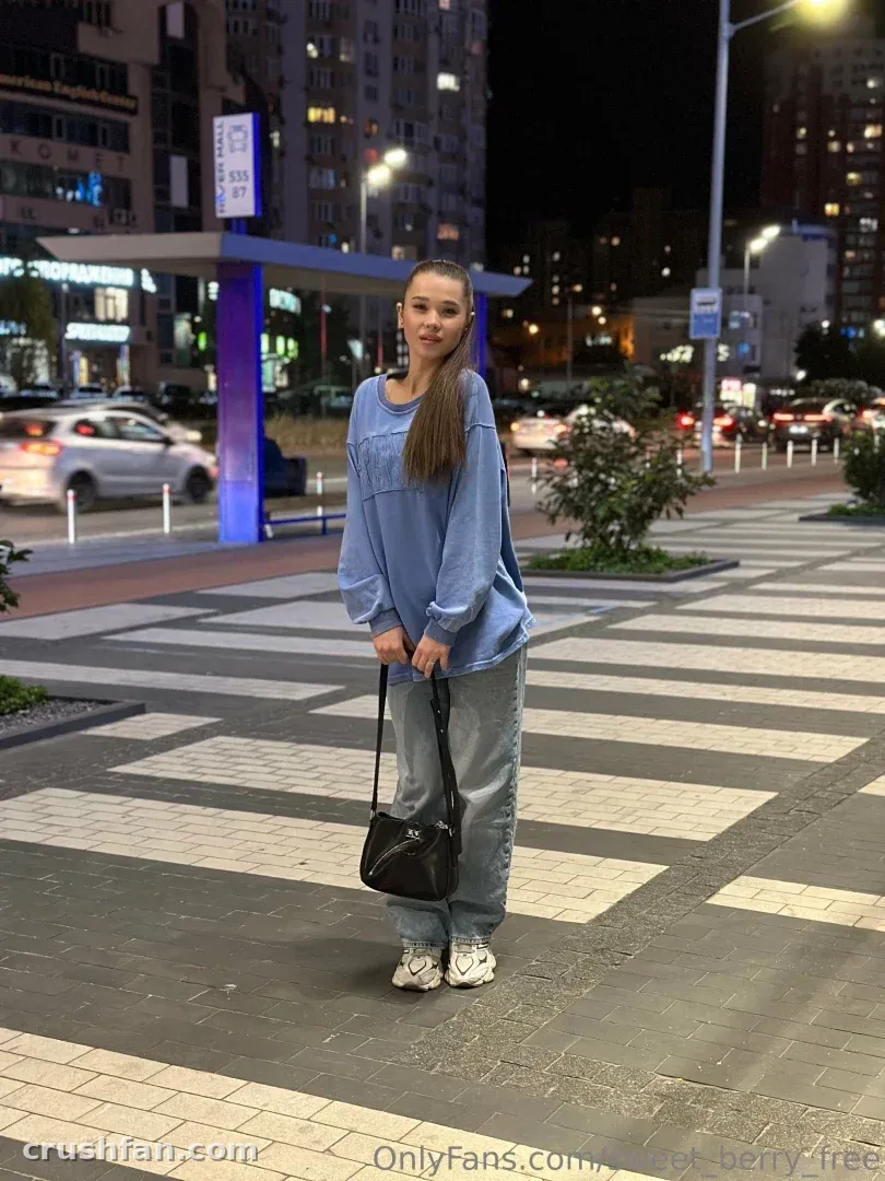 Sweet Berry dans un haut et un pantalon bleus debout sur une allée urbaine la nuit