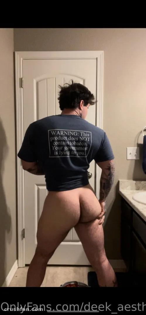 DEEK AESTHETIC con una camiseta gráfica oscura de pie en un baño junto a una puerta blanca