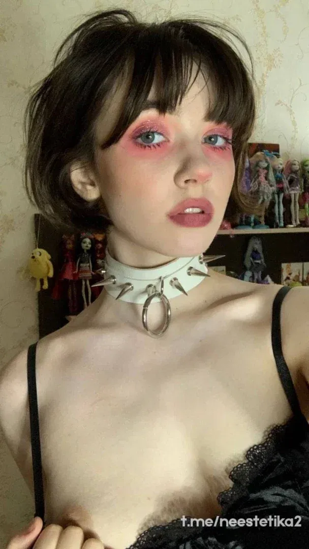 Katyusha wearing a spiked white choker and black lace top, with figurines on a shelf behind her.