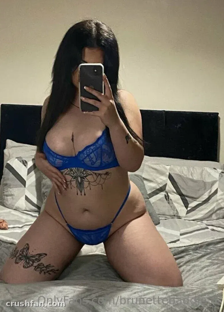 Olivia Mae стоит на коленях на кровати в синем кружевном белье и делает селфи в зеркале