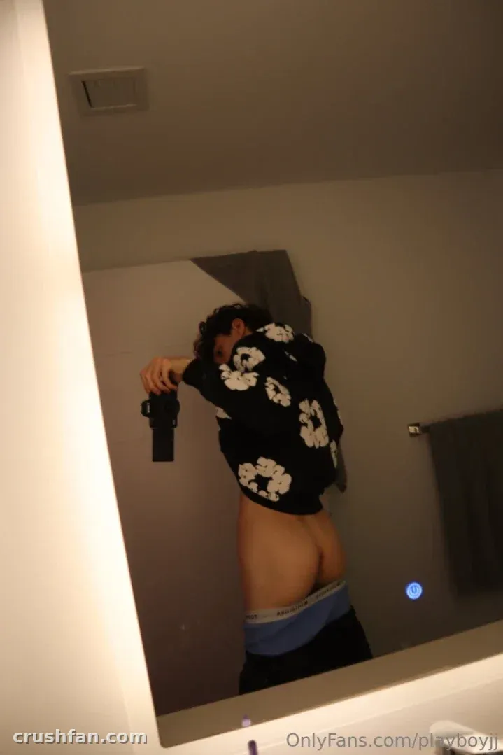 Jayden in a dark floral shirt taking a mirror selfie in a softly lit bathroom