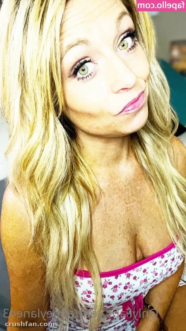 Abbey Lane inclina a cabeça em uma selfie de close, vestindo um top floral branco com acabamento rosa.
