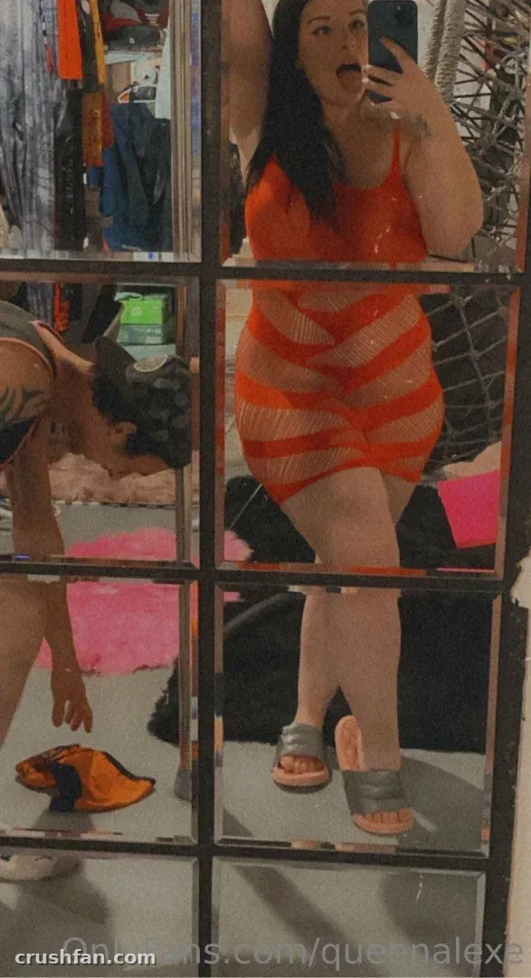 Queenalexe in an orange striped dress taking a mirror selfie in a room with a closet.