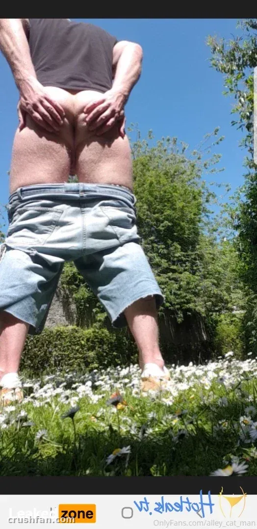 Person in dark shirt and denim shorts standing in a daisy-filled garden under a blue sky