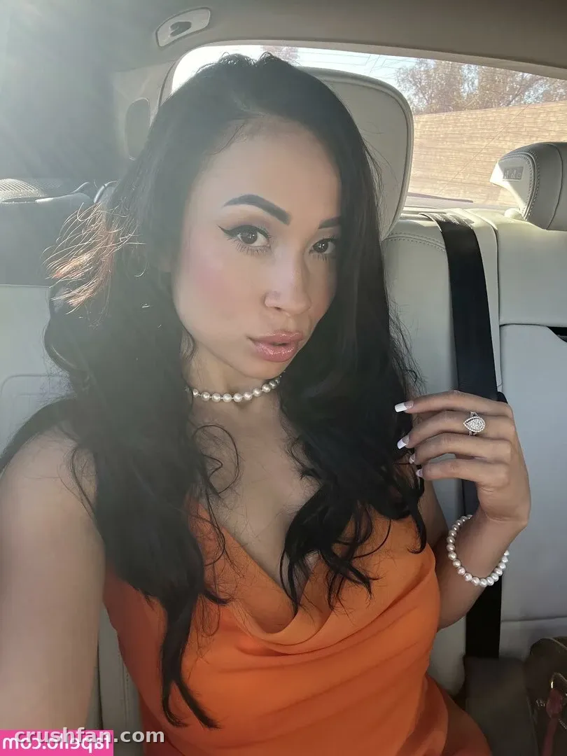 Créatrice avec un haut orange et des bijoux en perles posant à l'intérieur d'une voiture à la lumière du jour