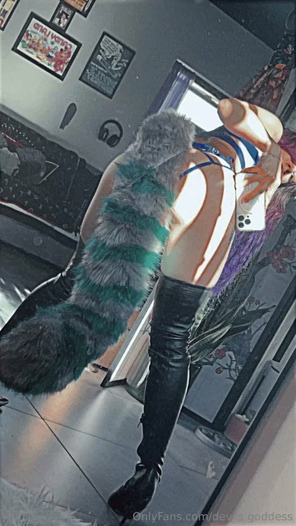 Tovi macht ein Spiegel-Selfie mit oberschenkelhohen Stiefeln und einem gestreiften Schwanz in einem Raum mit Postern.