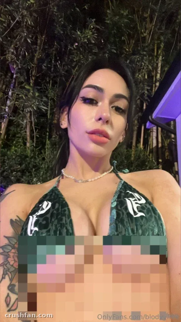 Blodvy in a green halter top outdoors at night with tattoos visible.