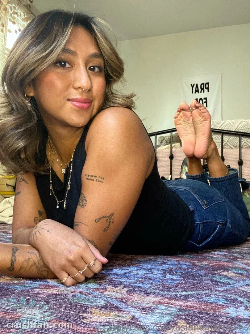 Asian Smart Soles deitada em uma colcha estampada com blusa preta e jeans